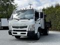 A 2015 Mitsubishi Fuso FE truck with a flatbed and drop sides is parked in a lot featuring a white body and multiple front lights