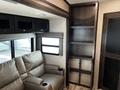 A 2021 Grand Design Recreational 311BHS with a light brown leather sofa featuring cup holders and a tall storage unit with open shelves and a mesh compartment