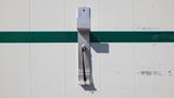 A metallic latch mechanism mounted on a white surface with a horizontal green stripe