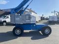A 1997 Genie S-65 4X4 lift in side profile displaying a blue and gray metallic finish with large tires and a raised boom arm