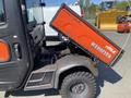 A 2018 Kubota RTV-X 1100 C utility vehicle with an orange and black color scheme and a cargo bed tilted upward for dumping contents