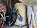 A blue fuel nozzle attached to a hose next to a large white barrel on a truck