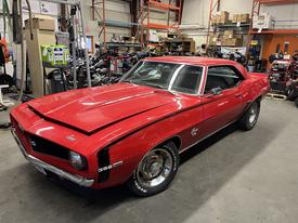 A red 1969 Chevrolet Camaro with a sleek body design and prominent hood lines features black racing stripes and white-letter tires