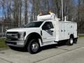 A white 2018 Ford F-550 with a large utility service body and orange lights on top ready for work
