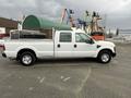 A white 2010 Ford F-250 SD pickup truck with a flatbed and a toolbox in the truck bed viewed from the side