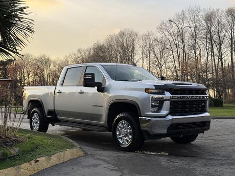 A 2023 Chevrolet Silverado 3500HD in silver with chrome accents parked on a driveway showcasing its large wheels and bold front grille