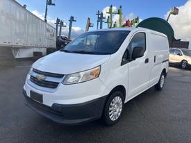 A 2015 Chevrolet City Express van in white with sliding side doors and a black front grille parked with its headlights on