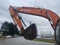 A 2006 Hitachi ZX200LC excavator with a large bucket attached is positioned prominently, its arm raised and ready for operation