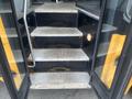 Three metal steps leading up into a bus with a yellow exterior and black accents
