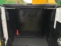 An open black storage compartment with hooks on the back wall and a small red device on the left side