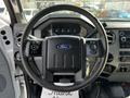 A black steering wheel with a Ford logo is in focus with various controls on the sides and a dashboard with gauges visible in the background