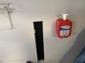 A red hand sanitizer dispenser mounted on a wall near a black rectangular opening