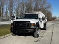 A white 2008 Ford F-450 SD with a black front grille and utility bed attached driving on a pavement