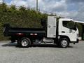A 2015 Mitsubishi Fuso FE flatbed truck with a white cab and black loading area is positioned sideways on a paved surface