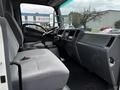 Interior of a 2018 Isuzu NRR showing the driver's seat dashboard and steering wheel with a grey fabric upholstery and controls visible