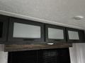 A set of three upper cabinets with frosted glass doors and dark wood frames inside a 2022 Aspen Trail recreational vehicle