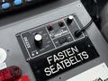 A control panel featuring buttons and switches labeled for various functions including speakers and power with a large sign reading FASTEN SEATBELTS