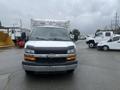 A 2016 Chevrolet Express van in the foreground with a gray body and black accents facing forward