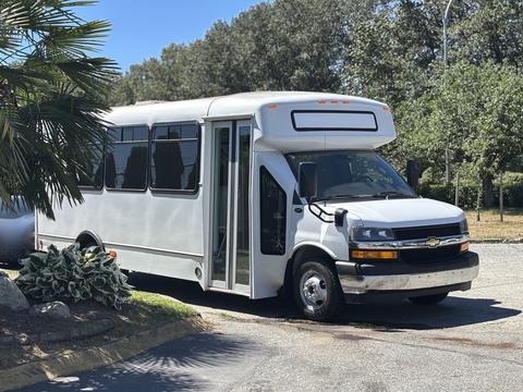 A 2020 Chevrolet Express bus with a white exterior and large windows parked with its door open