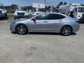 A 2017 Acura TLX sedan in silver parked on a lot with trucks in the background, showcasing its sleek design and alloy wheels
