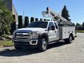A 2016 Ford F-550 truck with a mounted aerial lift and a utility bed featuring multiple compartments on the side