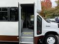 A white and brown 2014 Ford Econoline shuttle bus with an open door revealing the interior seating and steps leading inside
