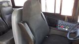 A grey driver's seat inside a 2014 Freightliner Thomas diesel bus with controls and buttons on the side panel