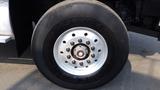 Close-up of a large black tire mounted on a white wheel with multiple bolt holes and a center hub on a truck