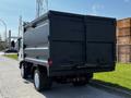A 2016 Isuzu NPR truck with a black dump bed is parked on the side of the road