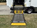 A metal wheelchair ramp extending from the back of a 2020 Chevrolet Express with a yellow and black design