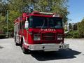 A red 2006 Emergency One Fire Truck with a prominent "FIRE DEPT" label on the side, featuring lights, a rear hose compartment, and chrome accents