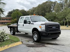 A 2015 Ford F-350 SD truck with a white exterior and flatbed in the foreground