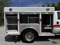 A 2009 Ford F-550 with open storage compartments on the side featuring red stripes and metal shelving inside
