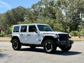 A white 2021 Jeep Wrangler Rubicon parked with black wheels and rugged tires