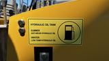 A yellow sign mounted on machinery indicating the hydraulic oil tank with instructions for summer and winter oil use