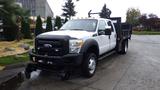 A 2011 Ford F-550 flatbed truck with a white exterior and black front grille parked on a driveway