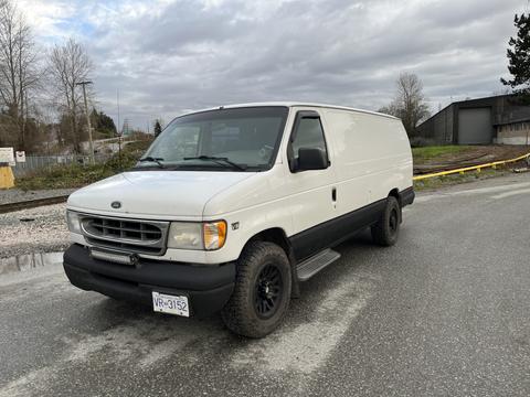 A white 2001 Ford Econoline van with black wheels parked on a gravel surface