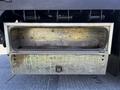 A metal storage compartment beneath a 2012 Freightliner M2 112 truck with a rusty interior and a latch on the front