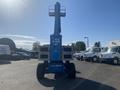 A blue 1997 Genie S-65 4X4 aerial work platform with a raised boom and large tires positioned facing the viewer