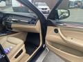 Interior of a 2009 BMW X5 featuring a cream leather seat and wood trim dashboard with a passenger door open and a bottle of water in the cup holder