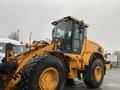 A 2016 Hyundai HL940 wheel loader with large tires and an orange exterior, featuring a cab with glass windows and controls visible inside
