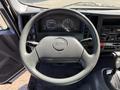 A gray steering wheel of a 2013 Isuzu NPR showing the logo and controls on either side with gauges visible in the dashboard behind it