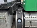 Close-up view of a 2013 Kenworth T370 truck featuring a chrome exhaust pipe and a green cab with visible mechanical components and a storage compartment