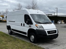 A white 2021 RAM Promaster van parked on a grassy area with a plain exterior and a RAM logo on the front grille
