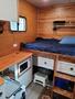 Interior of a 2022 Royal Camper featuring a bed with navy bedding a kitchenette area with a microwave and storage drawers