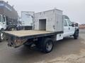 A white 2009 Ford F-450 SD flatbed truck with a metallic storage box in the bed and dual rear wheels