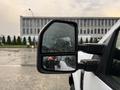 A 2017 Ford F-350 SD side mirror with raindrops on it reflecting part of the vehicle and a person taking a photo