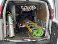 A 2014 GMC Savana van interior filled with various tools and materials including pipes ladders and a gas cylinder