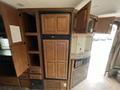 A 2013 Outdoor Wind River kitchen area featuring a wooden refrigerator with panel doors along with several storage cabinets and a small countertop space