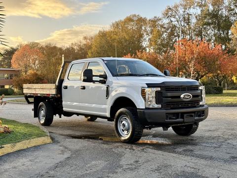 A 2018 Ford F-350 SD with a flatbed is parked at an angle showcasing its front and side view with a sturdy build and large tires